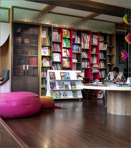 Inside view of School library with  books arranged on the shelves and three staff sitting on the table and three more sitting down and reading