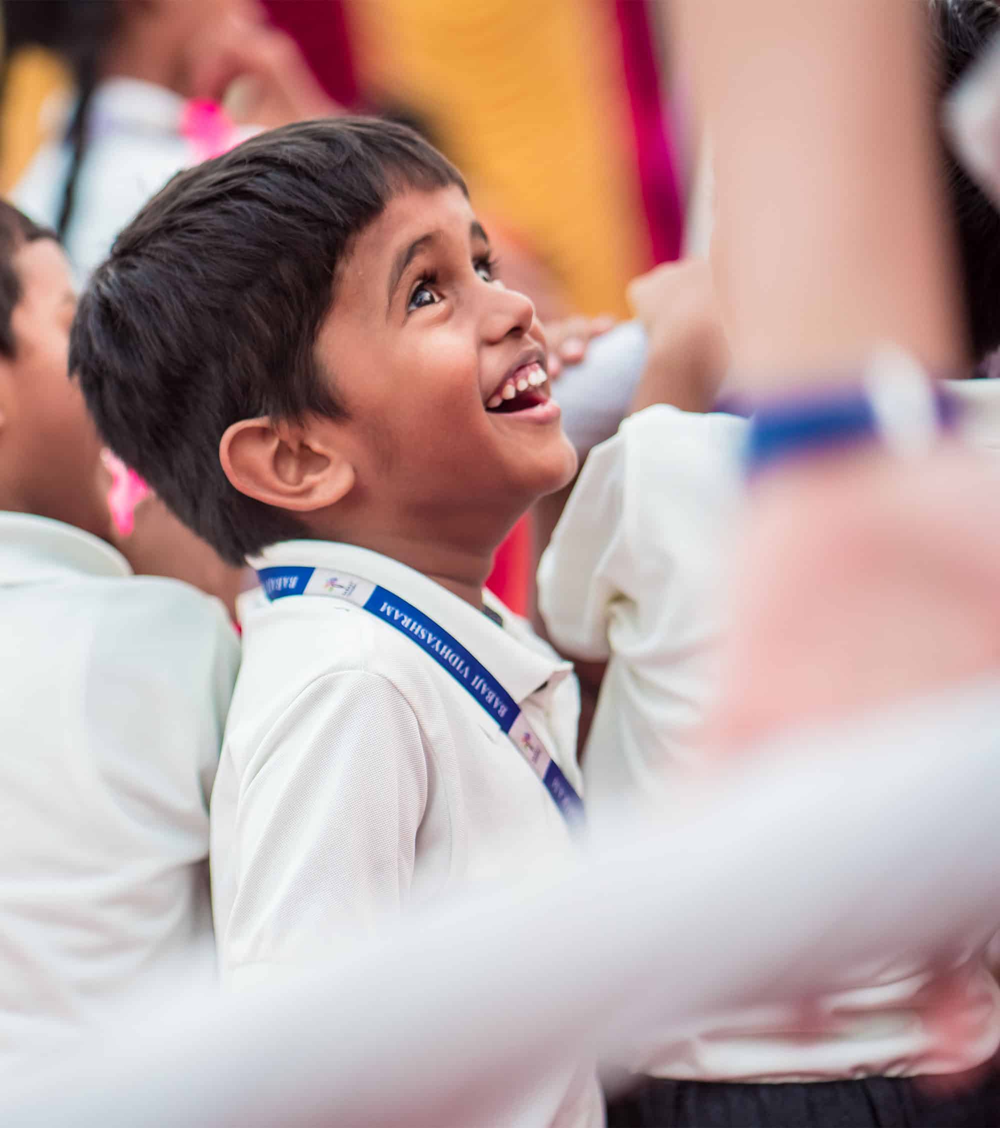 Happy Babaji Vidyashram School boy child seated in a classroom looking up and smiling.